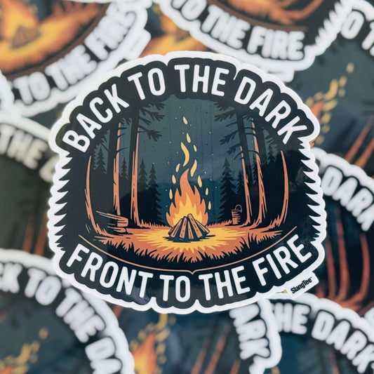 Stack of 'Back to the Dark, Front to the Fire' themed stickers with a central design of a campfire and trees.